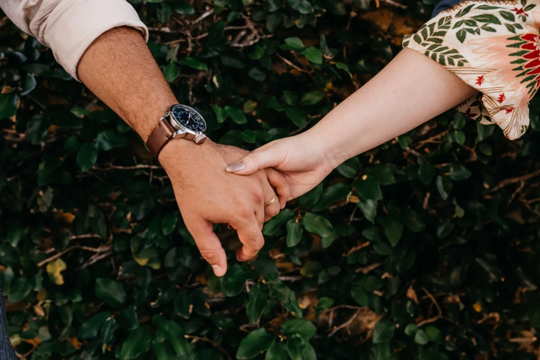 Two people holding hands against soft green leaves
